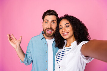 Happy young couple taking a cheerful selfie against a vibrant pink background