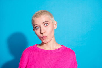 Stylish young woman with short blond hair poses against a vibrant blue background, expressing surprise