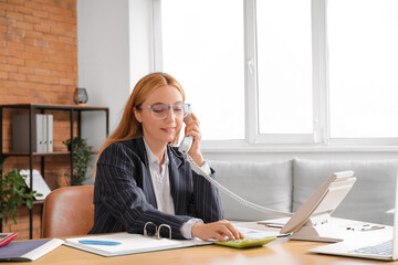 Wall Mural - Female accountant talking on phone and working with documents at workplace in office