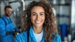 ©  Jovaduplex - A woman in a blue uniform smiles warmly at the camera, standing in a work environment with a blurred coworker in the background, symbolizing occupational harmony.
