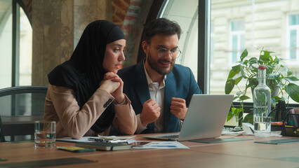 Two multiethnic business partners colleagues male female workers man muslim woman in hijab at table office Arabian Indian businessman businesswoman looking at laptop computer screen wait expect result