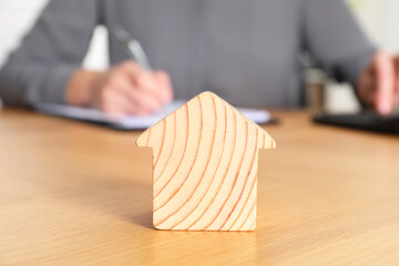 Poster - Property insurance. Real estate agent working at table indoors, focus on wooden house figure