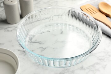 Glass casserole and other cooking utensils on white marble table, closeup