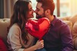 © indofootage - Happy Valentine's Day. Young couple in love holding a heart-shaped balloon while sitting on the sofa in the living room. Macro shot