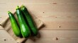 © yut - Three vibrant green courgettes arranged on a rustic burlap cloth atop a light wood surface, offering a fresh and healthy culinary image.