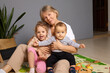 © sementsova321 - A grandmother sits on a play mat surrounded by her two grandchildren, smiling and engaging in playful activities. The warm atmosphere highlights family bonding and joy