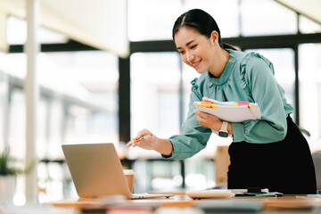 Wall Mural - Asian female employee holding documents to check information Managing annual financial and tax analysis documents