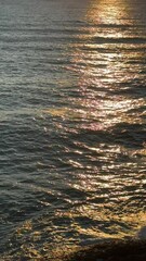 Wall Mural - Glittering sea waves with golden sun reflections on surface at evening, vertical video.