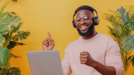 Wall Mural - a man in a yellow shirt is wearing headphones and smiling while using a laptop. concept of happiness