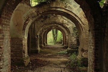 Poster - Abandoned structure with weathered arches and exposed brick walls at sunset in a deserted location