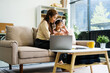 © NanSan - An Asian mother and her adorable daughter sit on the sofa in their living room, enjoying online learning on a tablet and reading books. A joyful family moment focused on education