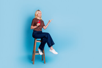 Wall Mural - Photo of lovely cheerful woman wear trendy clothes sitting wooden chair look empty space isolated on blue color background