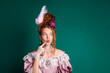 © deagreez - Elegant young woman in vintage costume with red hair and glamorous jewelry against a green background