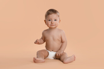 Wall Mural - Cute little baby in diaper sitting on beige background