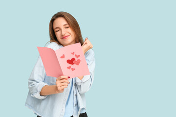 Wall Mural - Beautiful young woman holding greeting card with hearts on blue background. Valentine's Day celebration