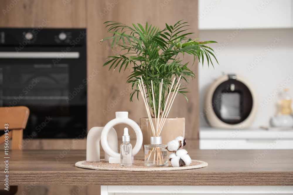 Reed diffuser with cotton flowers, essential oil and plant on table in kitchen, closeup
