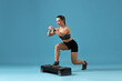 © New Africa - Woman in gym clothes doing exercise with step platform on light blue background