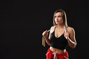 woman in gym clothes with skipping rope on black background, space for text