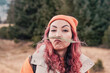 © EdNurg - Funny young woman with pink hair, using grass as a fake mustache, enjoying the mountain landscape