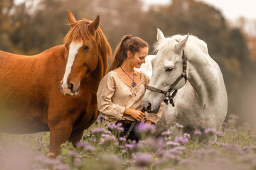 Wall Mural - Horsemanship concept: A woman interacts with her two horses at a flower field in autumn outdoors