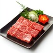 © sopix - Raw marbled beef cubes on a dark rectangular plate garnished with cucumber, tomato, and herbs.