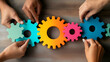 © Pukan - Hands assembling colorful gears on a wooden surface, symbolizing teamwork and collaboration in a creative or educational context.