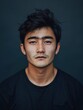 © djatu - Close-up portrait of a young Asian man with dark hair and a serious expression, wearing a black t-shirt against a dark background.