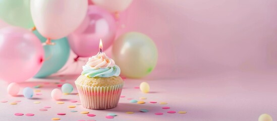 Festive cupcake with candle and pastel balloons on pink background.