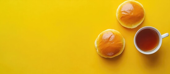 Aufkleber - Two classic buns and a cup of tea on a vibrant yellow background aerial view with plenty of empty space for text or design use