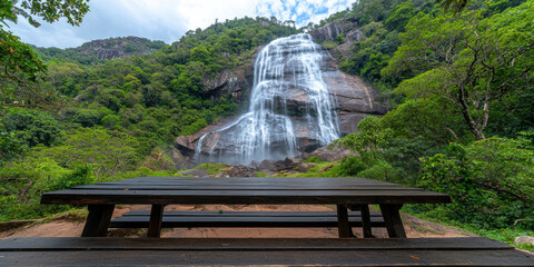 Wall Mural - A serene waterfall cascades down a lush green hillside, with a wooden picnic table set in the foreground for visitors to enjoy the natural beauty.