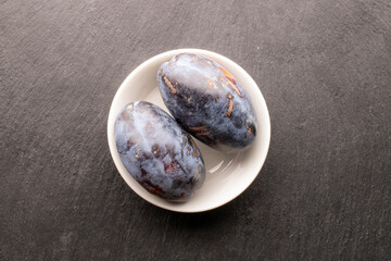 Wall Mural - Black ripe plums with homemade kitchen utensils on slate stone, close-up, top view.