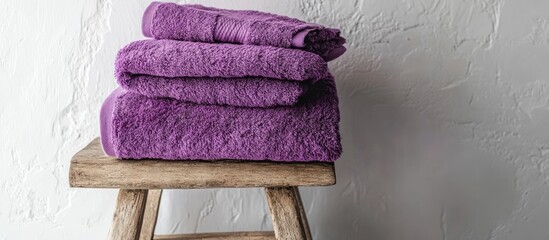 Leinwandbilder - Vibrant violet plush towels stacked on a rustic wooden stool enhancing bright white bathroom decor and interior design aesthetics