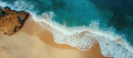 Poster - Scenic aerial view of gentle waves lapping against a sandy beach with rocky formations in a serene coastal environment
