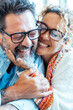© simona - An adult couple in their late 40s, wearing glasses, smiling and embracing each other with joy while looking at the camera, enjoying a positive moment of their married life, filled with love and happy