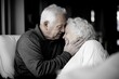 © Milos - An elderly couple share a tender embrace, their foreheads touching, capturing a beautiful moment of love and togetherness within their warm home environment.