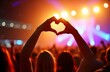 © Pete - Audience members at concert create heart shape with hands. Crowd enjoys live music performance at festival. Enthusiastic fans cheer, wave hands in air. Colorful lights highlight silhouettes of people