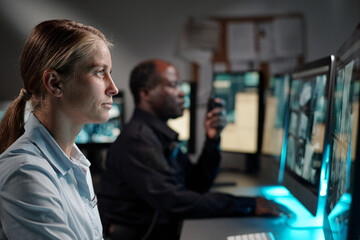 Poster - Side view of young blond woman in shirt looking at screen of desktop computer while watching cctv video from hotel reception