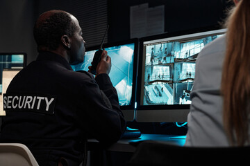 Poster - Mature African American man talking in radio transceiver and looking at computer screen with cctv video system