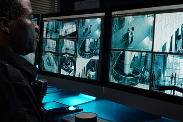 Poster - Serious African American security guard watching cctv video in surveillance room while observing hotel life on computer screen