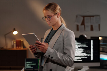 Poster - Blond young businesswoman with tablet looking at screen while decoding online data in front of camera in modern office