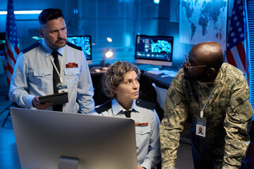 Aufkleber - Serious mature woman in uniform looking at young African American male officer during discussion in front of desktop computer