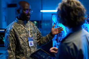 Aufkleber - Confident African American man in camouflage uniform pointing at interactive screen with army location during discussion