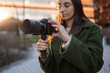 © ADDICTIVE STOCK - Woman in green coat holding camera outdoors at sunset