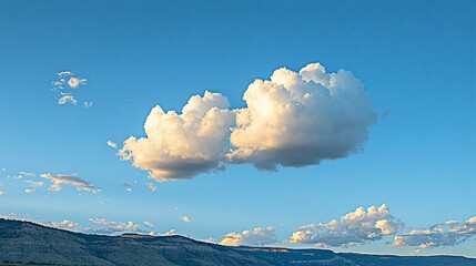 Poster - Two fluffy cumulus clouds float in a vibrant blue sky above a distant mountain range at sunset.