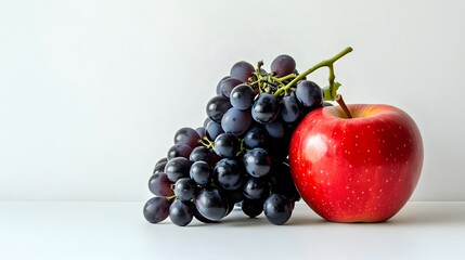 Wall Mural - A vibrant red apple rests beside a bunch of dark purple grapes on a bright white background.  A simple, yet striking still life image of fresh fruit.