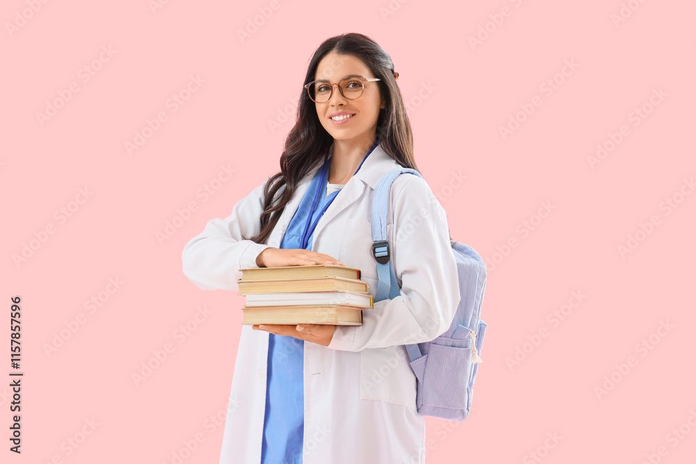 Young female medical student with books and backpack on pink background