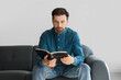 © Pixel-Shot - Man reading Bible while sitting on sofa at home