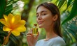 © Valentyna - Young woman holding a glass bottle of oil surrounded by tropical greenery and yellow flowers in a natural setting. Jojoba oil.