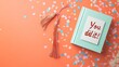 © Thavesak - Celebrating Academic Success - Open Book with Diploma, Confetti, and Encouragement Card on Pastel Orange Background