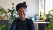 © Helga - A Blasian woman with a warm and approachable smile is seen working at her desk in a stylish, modern office. During a video conference with a client, her cheerful expression and eng